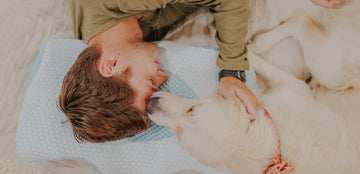 A man is lying on an Elviros memory foam pillow with his dog.